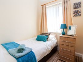 A bedroom with a single bed with pillows and towels next to a wooden dresser with a blue lamp and mirror at Haffannedd in Rhos-On-Sea