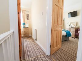 A hallway with striped carpet leading to a bedroom with a bed a dresser a wall-mounted tv and a chair at Haffannedd in Rhos-On-Sea