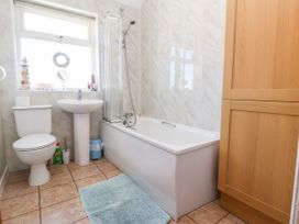 A bathroom with a toilet sink bathtub shower wooden cabinet and blue rug at Haffannedd in Rhos On Sea