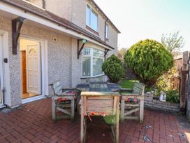 A patio area with wooden chairs and a table outside a house with a garden and bushes at Haffannedd in Rhos-On-Sea