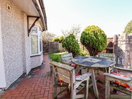 An outdoor patio with a wooden table and chairs on a brick floor next to a house and garden at Haffannedd in Rhos-On-Sea