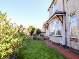 A garden area with green grass and shrubs beside a house with pebble dash walls and multiple windows at Haffannedd in Rhos-On-Sea