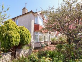 A front garden with trees shrubs a bench and a stone wall in front of a semi detached house at Haffannedd in Rhos On Sea