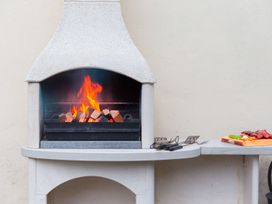 A fireplace with logs burning next to a cutting board at Carines Barns - Pol in Cubert