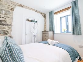 A bedroom with a bed with blue patterned pillows and a blue throw near a window with blue curtains next to a chest of drawers and a door with a white robe hanging Carines Barns - Pen Cubert