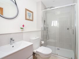 A bathroom with a sink, toilet, glass shower enclosure, round mirror, and framed artwork at Carines Barns - Pen in Cubert