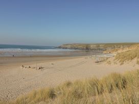 A sandy beach with grassy dunes and a small building near the shore at Carines Barns - Pen in Cubert