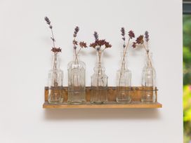 A wooden shelf holding glass bottles with dried flowers at Carines Barns - Wesley Barn, Cubert