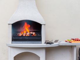 An outdoor fireplace with fire burning beside grill tools at Carines Barns - Wesley Barn, Cubert