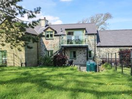 A stone and wood exterior of a two story house with a glass balcony and green grass lawn at Gwalia Cottage in Brynsiencyn