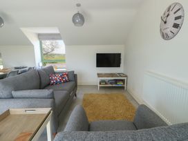 A living room with gray sofas a wall-mounted television a large clock and a yellow rug at Gwalia Cottage in Brynsiencyn