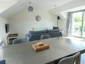 A living area with gray sofa dining table chairs wall clock and sliding glass door at Gwalia Cottage in Brynsiencyn