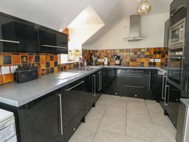 A kitchen with black cabinets gray countertops tiled backsplash and built-in oven at Gwalia Cottage in Brynsiencyn