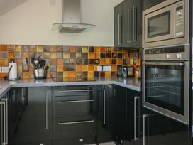A kitchen with black cabinets orange and yellow tiled backsplash stainless steel oven and microwave at Gwalia Cottage in Brynsiencyn