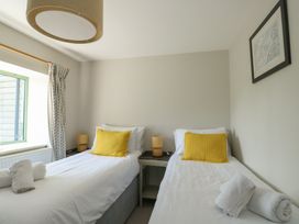 A bedroom with two single beds with yellow pillows and lamps on a bedside table at Gwalia Cottage in Brynsiencyn