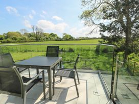 An outdoor balcony with black table and chairs overlooking a green field with trees at Gwalia Cottage in Brynsiencyn