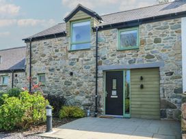 Exterior of a stone house with green framed windows a black door and garden plants at Gwalia Cottage in Brynsiencyn