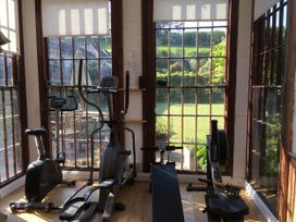 A gym with exercise equipment and windows opening to the garden at The Barn in Dittisham
