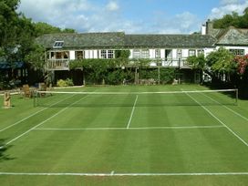 A tennis court with a building and seating area at The Barn in Dittisham