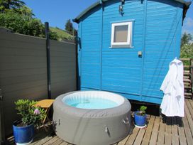 An inflatable hot tub on a wooden deck next to a blue wooden hut with a window two potted plants and a white robe hanging at Cuckoo at Wild Valley Huts in Llanrhaeadr-Ym-Mochnant