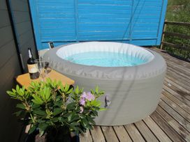 An inflatable hot tub on a wooden deck with a table holding a bottle of wine and two glasses and a potted plant next to it at Cuckoo at Wild Valley Huts in Llanrhaeadr-Ym-Mochnant