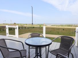 A deck area with a table and chairs overlooking grass and the sea at Bonny Bay Wilsthorpe near Bridlington