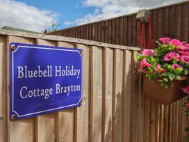 A sign for Bluebell Holiday Cottage Brayton attached to a wooden fence