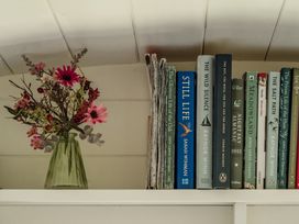 A shelf with flowers in a vase and various books at Hurdlemakers Hut Piddletrenthide