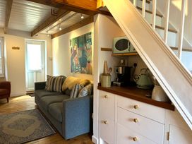 A living room with a gray sofa striped pillows wall art and kitchen appliances under stairs at Bodillys Cottage in Newlyn