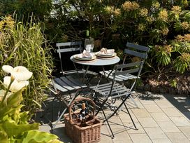 An outdoor patio with a round table set for two with plates and glasses surrounded by four metal chairs and a wicker basket with bottles of wine at Bodillys Cottage in Newlyn