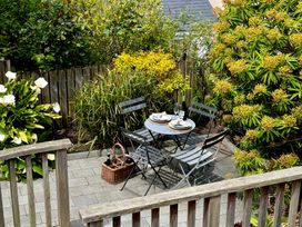 A small outdoor patio with a round table set for two surrounded by four chairs and plants at Bodillys Cottage in Newlyn