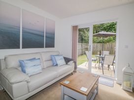 A living room with a leather sofa a wooden coffee table and patio doors leading to a garden at Ocean Retreat in Goodrington near Paignton