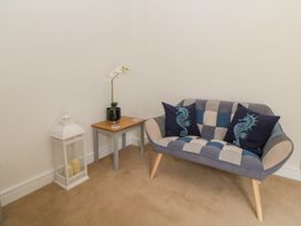 A corner with a small wooden table holding a potted orchid and coasters next to a patchwork loveseat with seahorse cushions at Ocean Retreat in Goodrington near Paignton