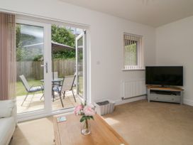 A living room with a wooden coffee table with flowers a TV on a stand and patio doors leading to an outdoor seating area at Ocean Retreat in Goodrington near Paignton