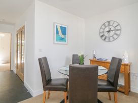 A dining area with a round glass table four brown leather chairs a wooden sideboard a wall clock and a framed sailboat print at Ocean Retreat in Goodrington near Paignton