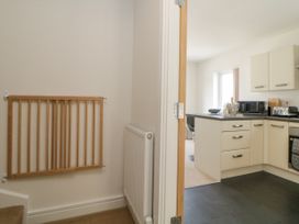 A kitchen with white cabinets and appliances viewed from a hallway with a wooden safety gate and radiator at Ocean Retreat in Goodrington near Paignton