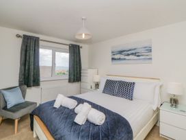 A bedroom with a double bed white bedding blue cushions bedside tables with lamps a grey chair by the window and wall art at Ocean Retreat in Goodrington near Paignton