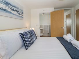 A bedroom with a bed with blue and white pillows a lamp and an open door showing a bathroom at Ocean Retreat in Goodrington near Paignton