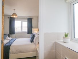 A bedroom with a bed and pillows next to a window with curtains and a small plant on a tiled windowsill at Ocean Retreat Goodrington near Paignton