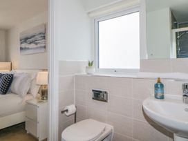 A bathroom with a toilet sink and window next to a bedroom with a bed lamp and bedside table at Ocean Retreat in Goodrington near Paignton