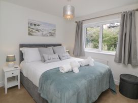 A bedroom with a bed covered with white and blue bedding a bedside table with a lamp and a window with curtains at Ocean Retreat in Goodrington near Paignton