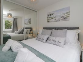 A bedroom with a double bed white and gray bedding bedside tables lamps and mirrored wardrobe doors at Ocean Retreat in Goodrington near Paignton