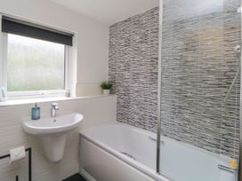 A bathroom with a sink soap dispenser bathtub shower and patterned wall tiles at Ocean Retreat in Goodrington near Paignton