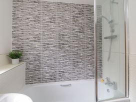 A bathroom with a bathtub shower combination and a potted plant on a shelf at Ocean Retreat in Goodrington near Paignton
