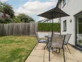 A patio with a table four chairs and an umbrella next to a grassy fenced garden at Ocean Retreat in Goodrington near Paignton