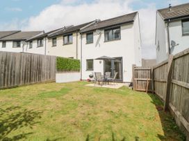 A fenced backyard with grass a patio table with umbrella and chairs outside a white house at Ocean Retreat in Goodrington near Paignton