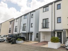 A row of modern three-story townhouses with parked cars on a paved street at Ocean Retreat in Goodrington near Paignton