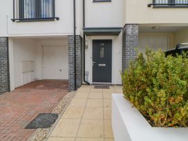 Front door with number 79 and welcome mat next to a driveway and garage with a plant in a white planter at Ocean Retreat in Goodrington near Paignton