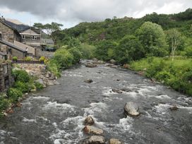 A river flowing alongside buildings and trees at Henfro in Beddgelert