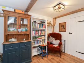 A snug with a bookshelf, armchair, and cupboard at The Old Byre in Woodfalls